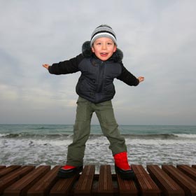 Young child making flying gesture on a seafront pier
